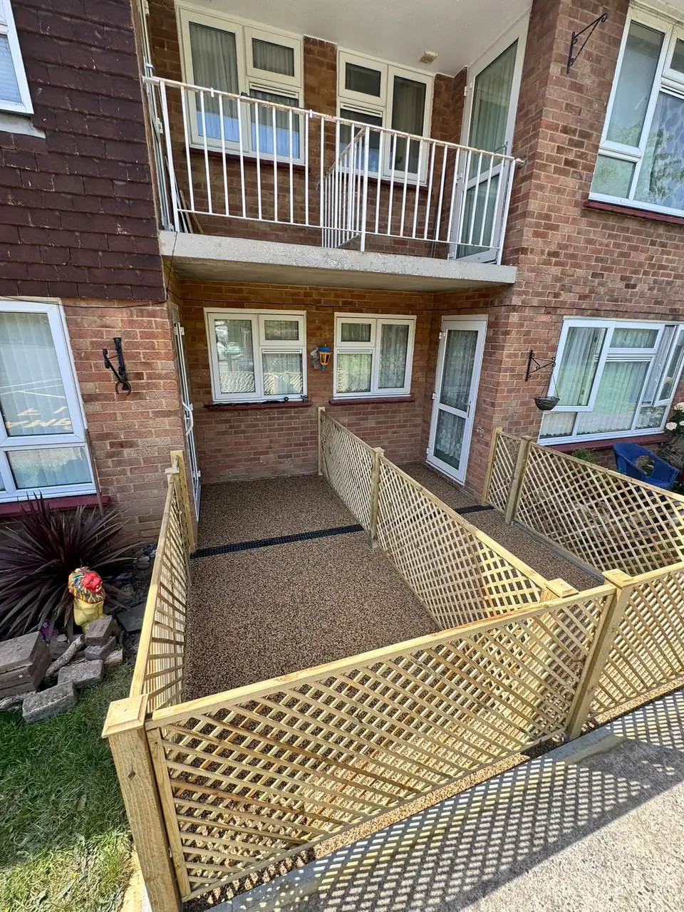 Finished aggregate surface and timber dividers beside a red-brick apartment building