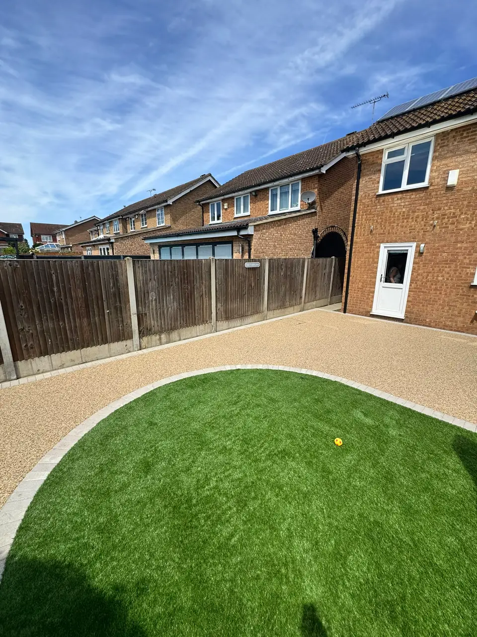 Second view of a finished tan resin-bound area around a curved green lawn
