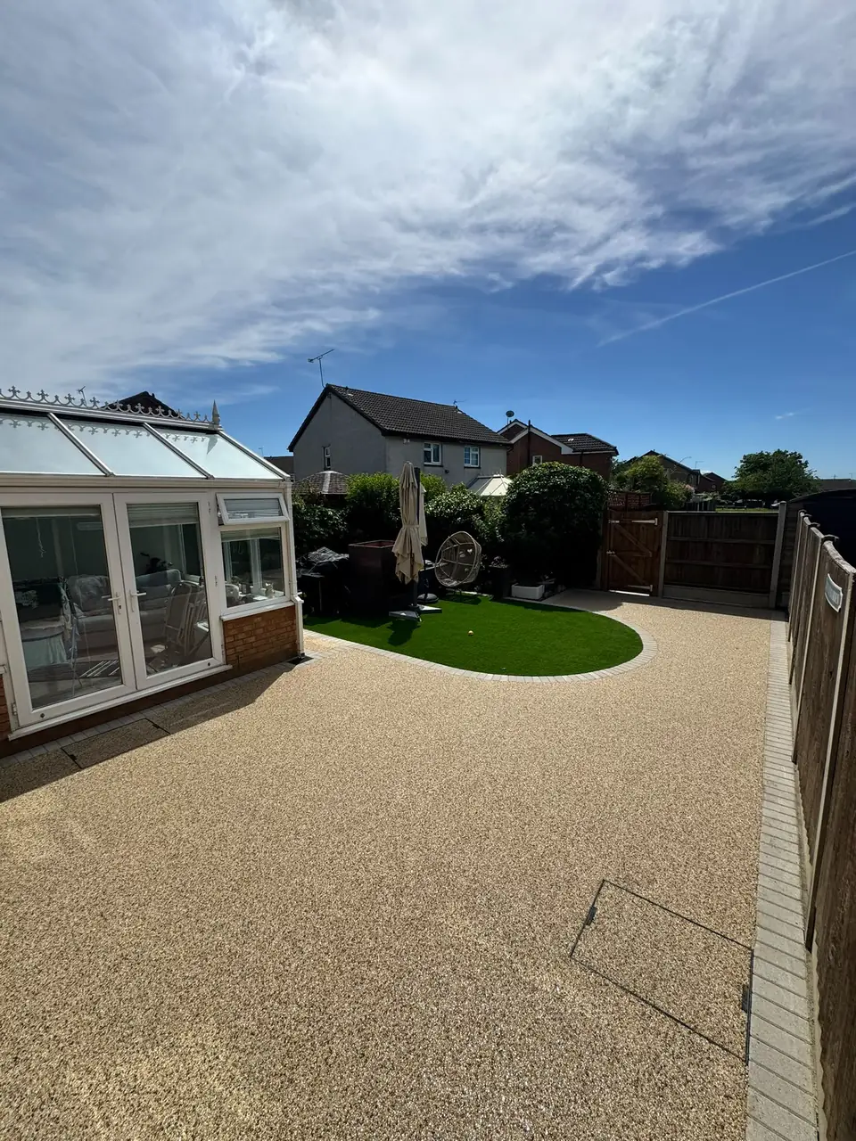 Pale resin-bound surface surrounding a curved artificial-lawn island beside the house