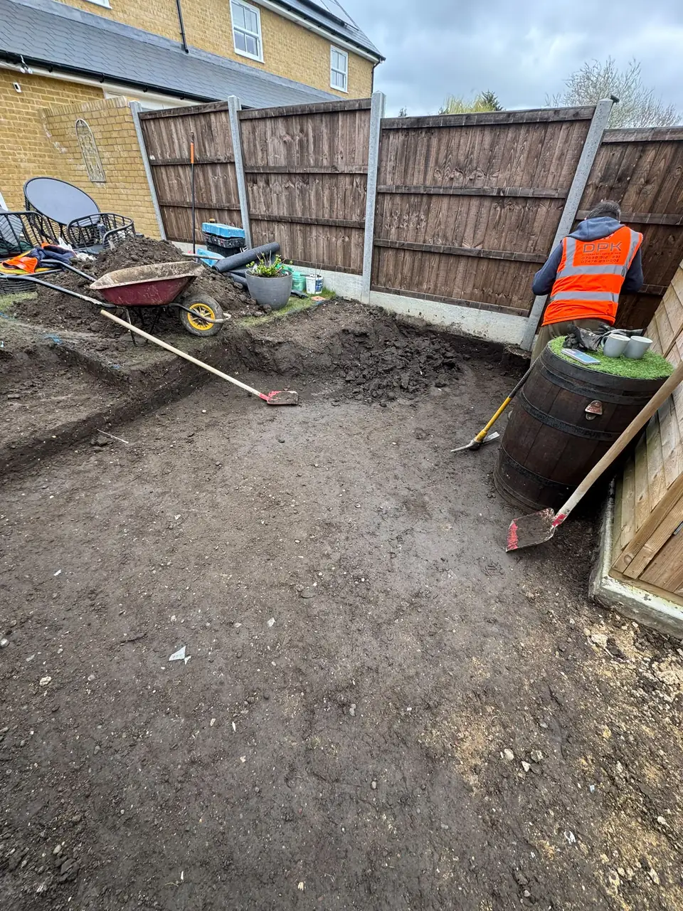 Excavated garden area with soil and tools during porcelain patio preparation