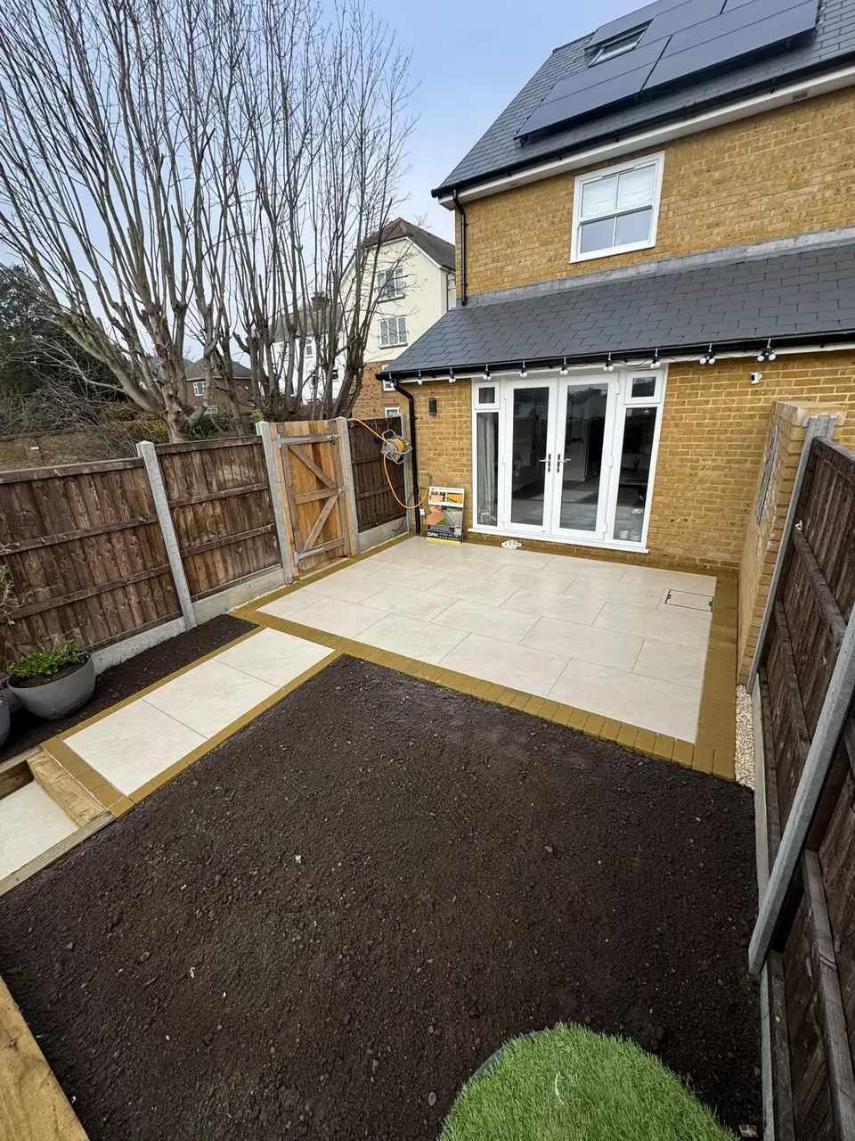 Porcelain patio beside the house with brick edging and garden soil