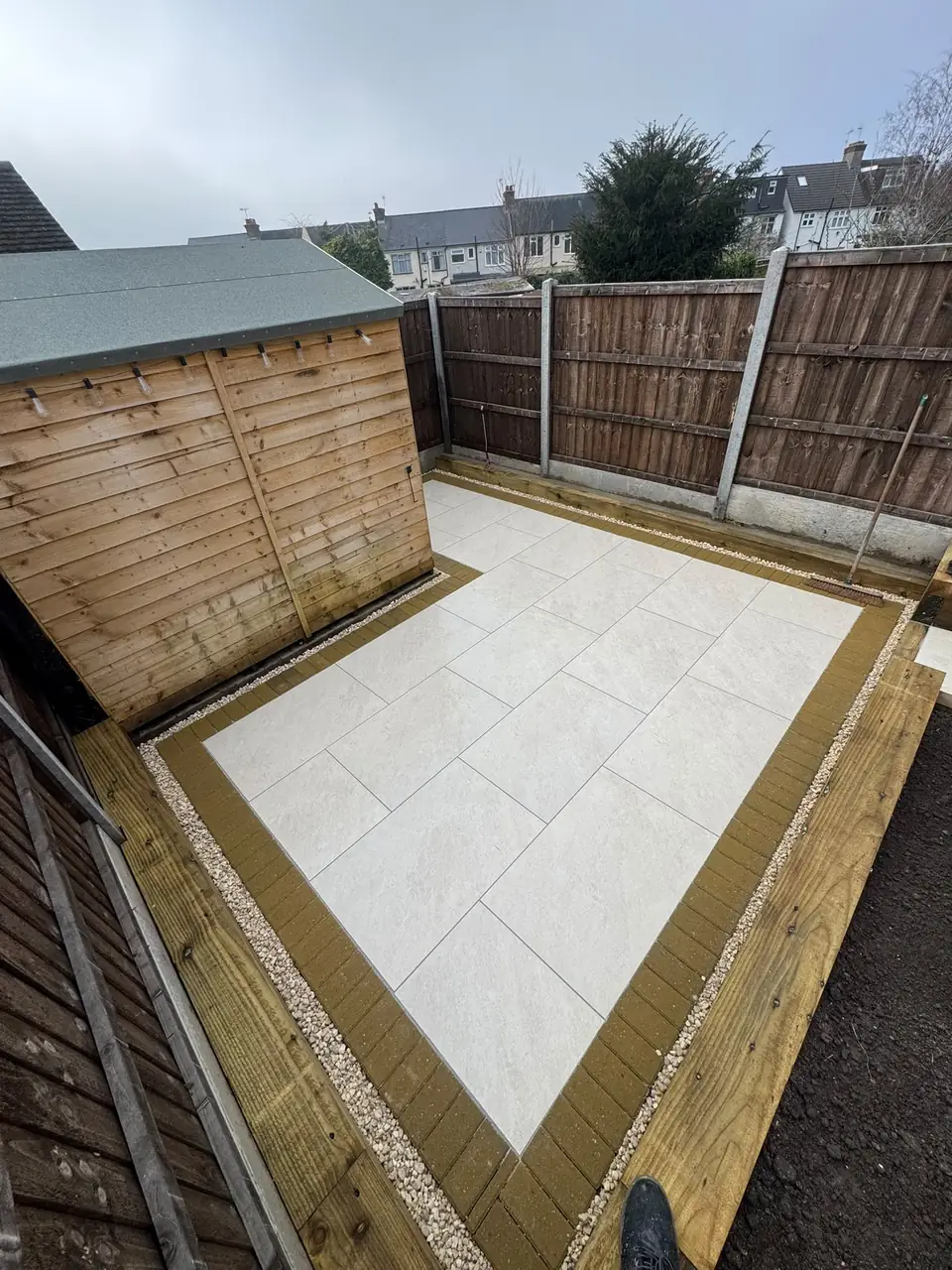 Pale porcelain paving with brick edging beside a garden shed